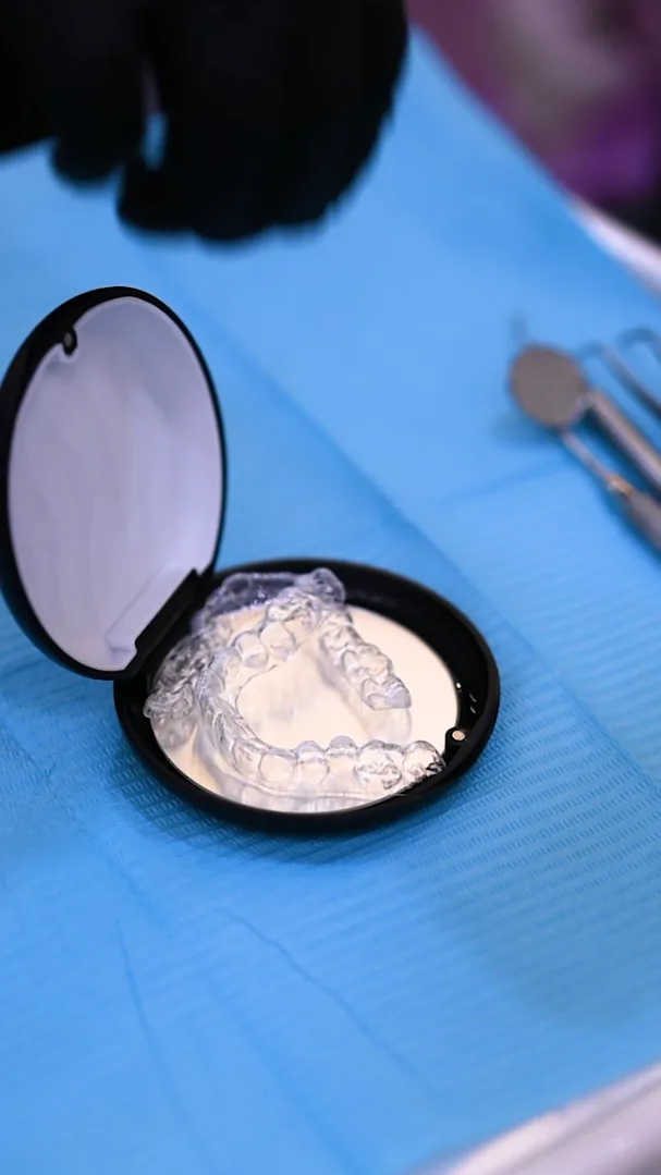 Upper and lower clear aligner trays in an open black case beside dental instruments