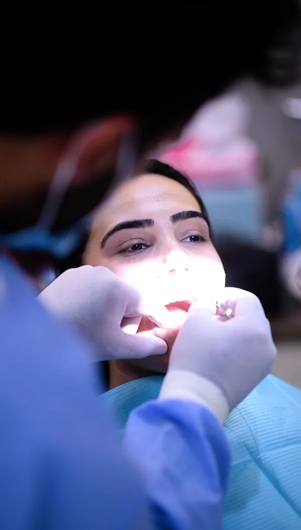 Gloved hands examining a woman's teeth under a bright dental light